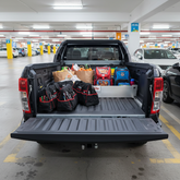 Truck bed with various items separated by a TubDivider including bags and groceries in a parking garage.