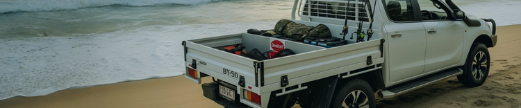 White pickup truck with a toolbox and camping gear seperated by a TrayDivider on a sandy beach near the ocean