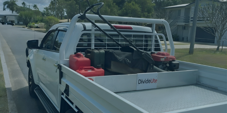 White truck with a flatbed carrying mowing equipment contained by a TrayDivider on a road.